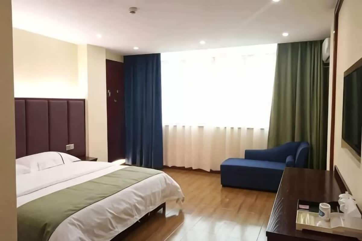 A hotel room with a bed, a desk, a chair, a window with curtains, and a television on the wall.