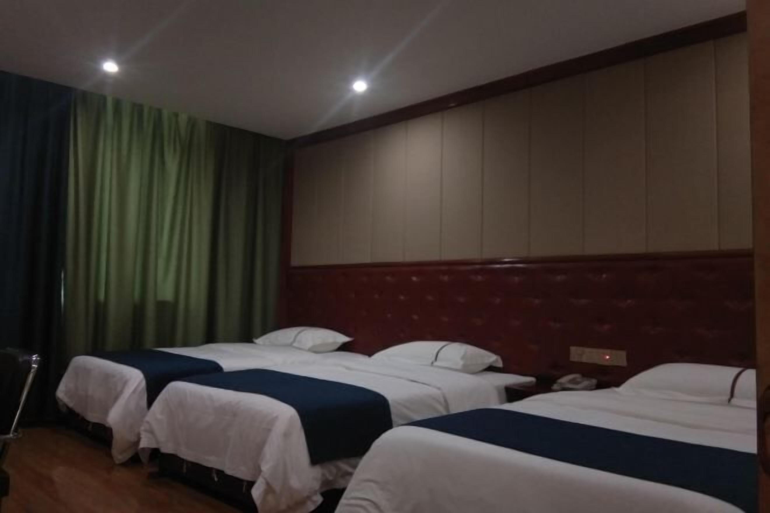 Habitación de hotel con tres camas, cabecera de madera y una cortina a un lado.