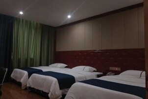 Habitación de hotel con tres camas, cabecera de madera y una cortina a un lado.