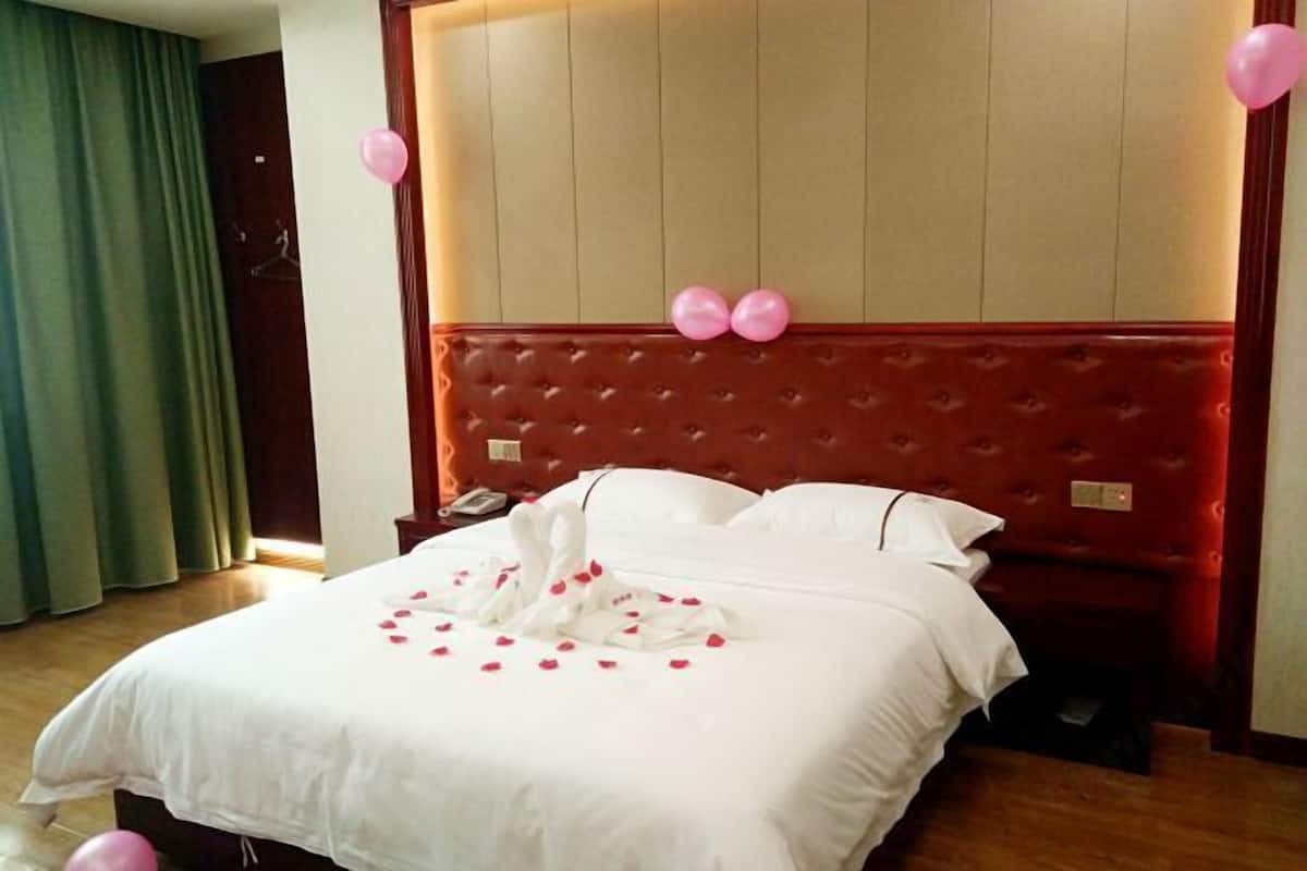 A hotel room with a large bed, a wooden headboard, and a nightstand.