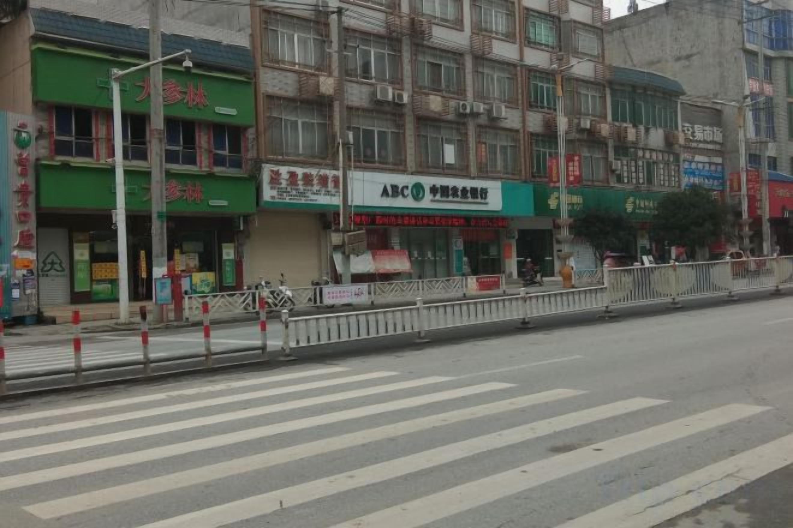 A street view with a crosswalk, storefronts, and a pedestrian fence.