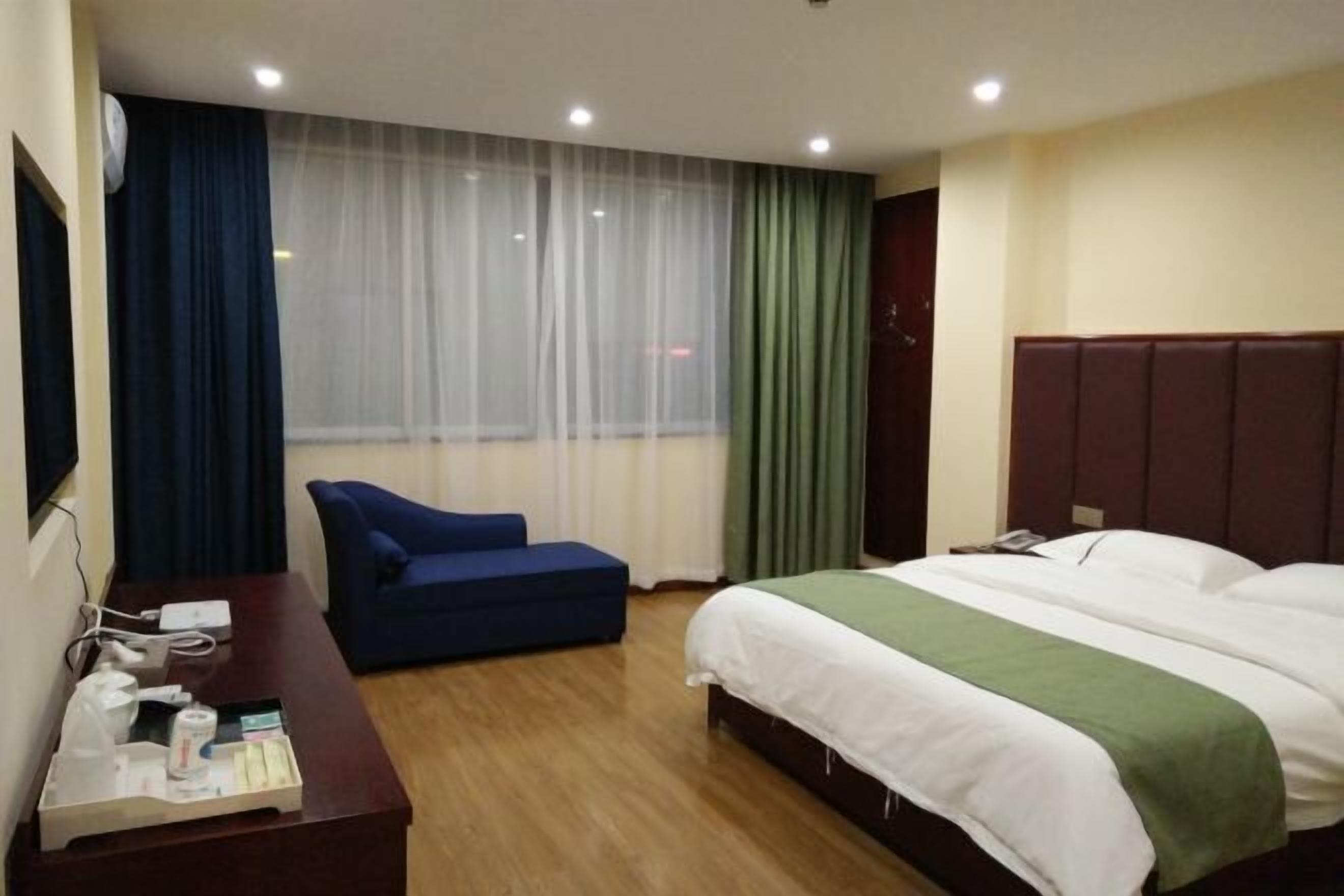 Habitación de hotel con cama, escritorio, silla, ventana con cortinas y televisión.