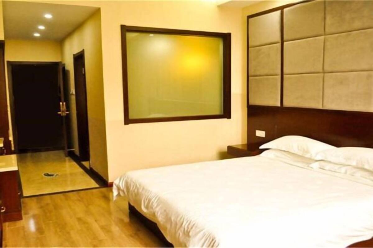 Una habitación de hotel con una cama, un ventanal grande, un cabecero de madera y una puerta.