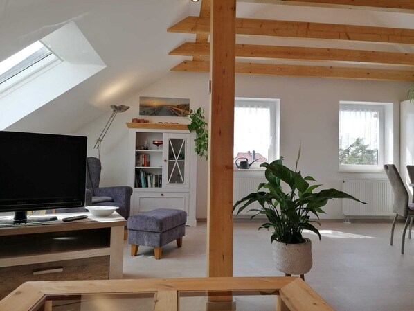 A modern living room with a TV, seating, a bookshelf, and a plant.