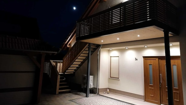 Een huis met twee verdiepingen, met een houten trap naar de bovenverdieping, een garage en een klein buitenruimte met een bankje.