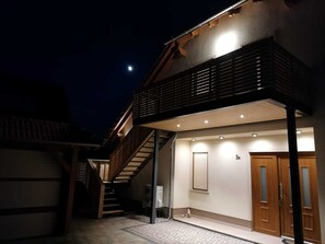 A two-story house with a wooden staircase leading to the upper floor, a garage, and a small outdoor area with a bench.