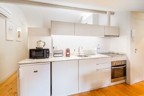A compact kitchen with white cabinets, a microwave, toaster, kettle, sink, and a small oven. - Oporto Loft with Mezzanine (Porto)