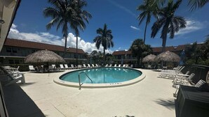 A pool area with lounge chairs and umbrellas, surrounded by palm trees. - 1BR Marco Island condo with pool, WiFi, kitchen, and heated pool. (Marco Island)