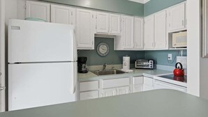A kitchen with white cabinets, a refrigerator, a sink, a toaster, and a kettle. - 1BR Marco Island condo with pool, WiFi, kitchen, and heated pool. (Marco Island)