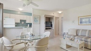A modern living room with a glass dining table, white chairs, a sofa, and a coffee table. - 1BR Marco Island condo with pool, WiFi, kitchen, and heated pool. (Marco Island)