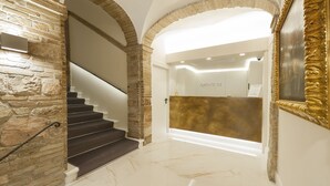 A modern interior with a marble staircase, stone walls, and a reception area with a gold accent wall. - Asisium Boutique Hotel (Assisi)