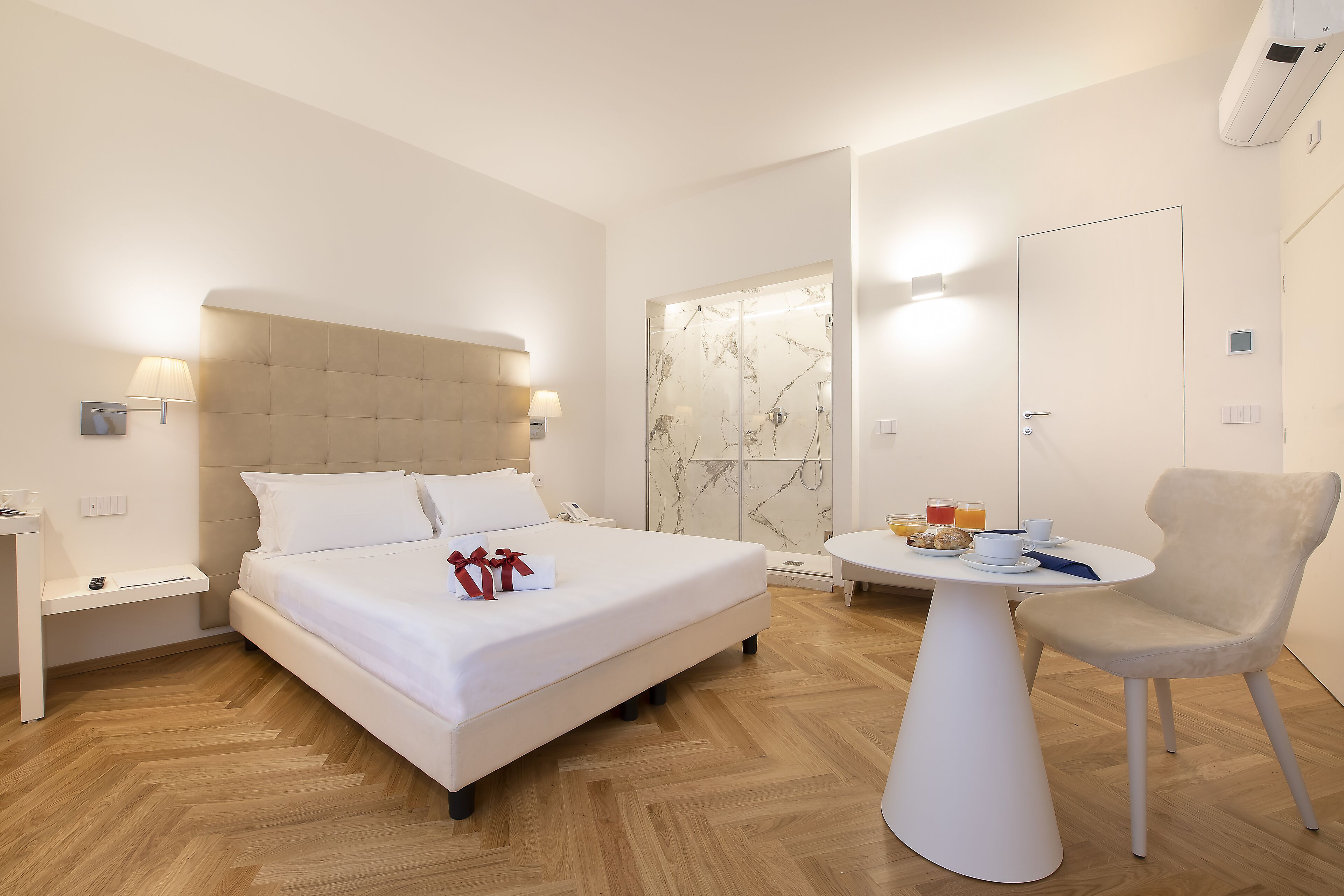 Une chambre d’hôtel moderne, dotée d’un grand lit, de tables de chevet, d’une petite table ronde avec une chaise et d’un espace douche.