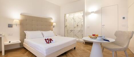 A modern hotel room with a large bed, bedside tables, a small round table with a chair, and a shower area.