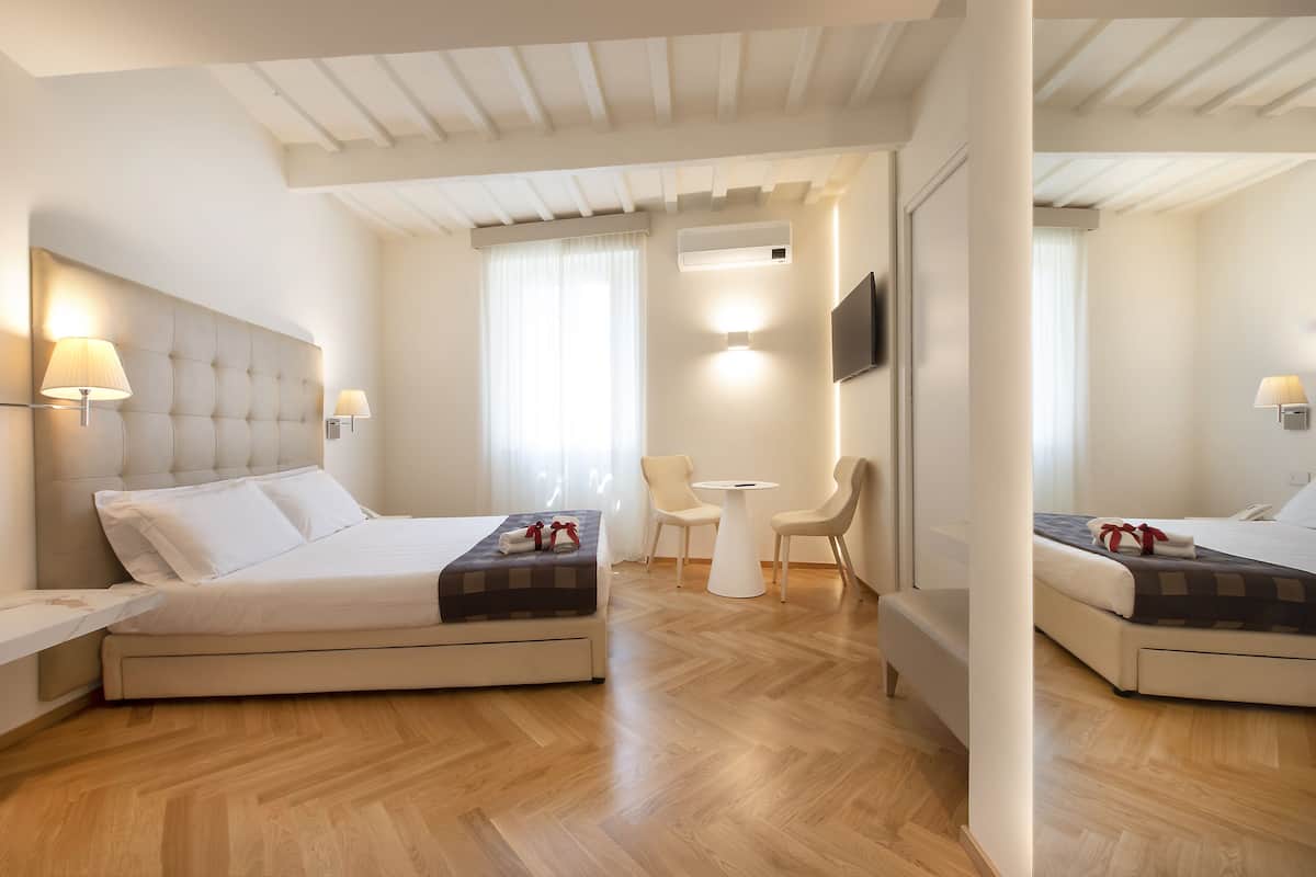 A hotel room with two beds, a desk, a chair, a TV, and an air conditioning unit.