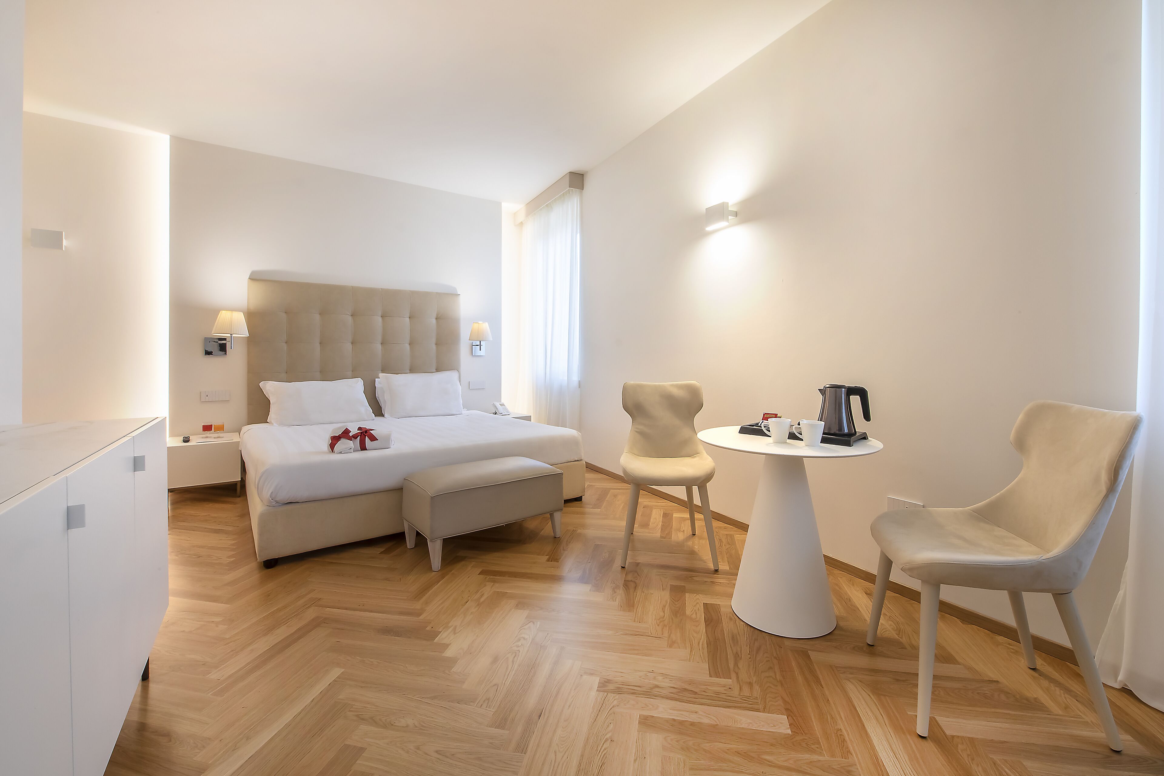 A modern hotel room with a bed, a chair, a small table, and a nightstand.
