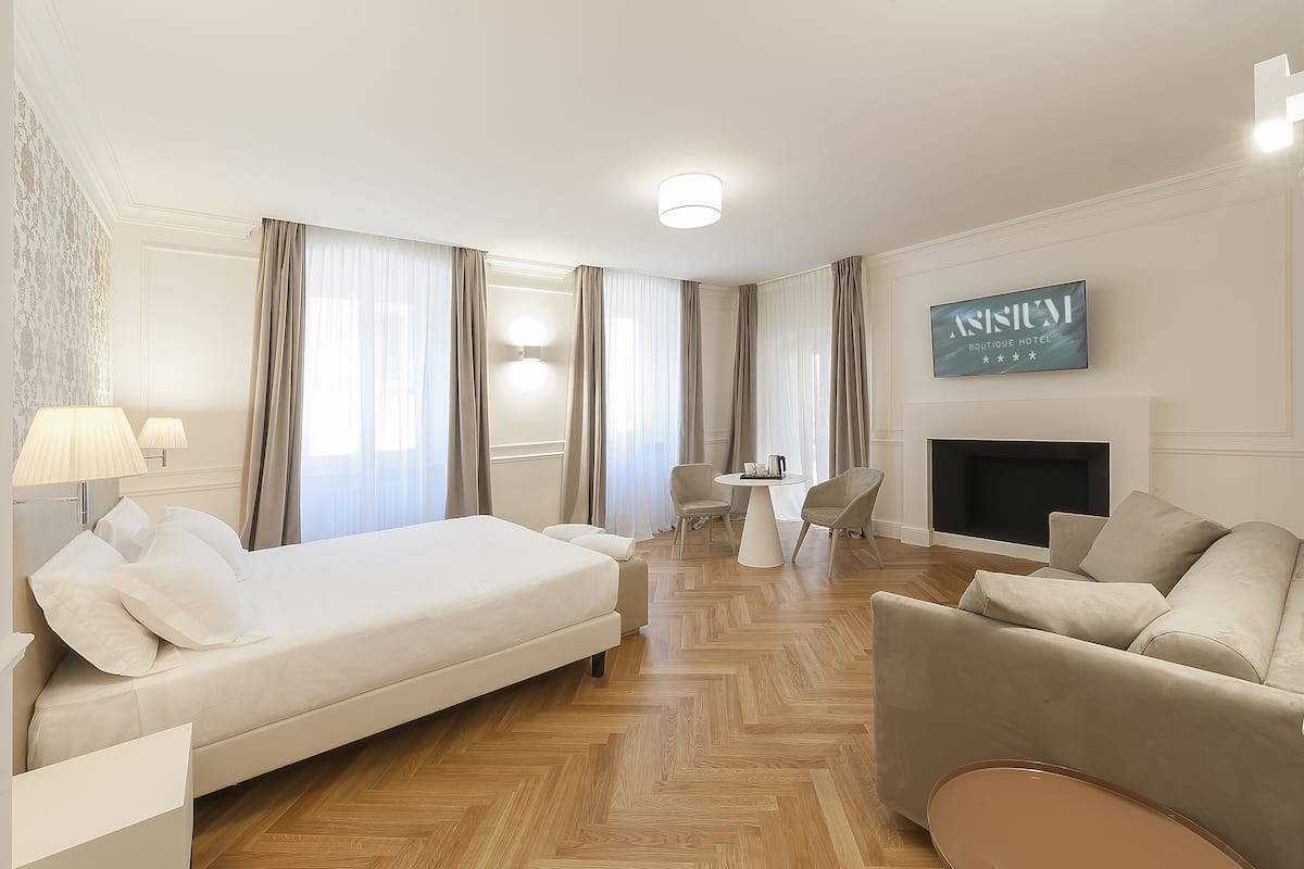 A hotel room with a bed, two armchairs, a small table, a fireplace, and a wall-mounted sign.