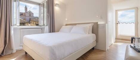 Habitación de hotel con una cama grande, una ventana con cortinas, un radiador y vistas a edificios.