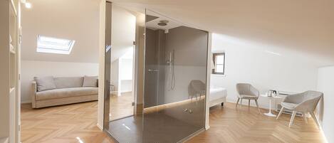 A modern, well-lit room with a glass-enclosed shower, a sofa, and a small table with chairs.