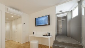 A modern bathroom with a shower, a toilet, and a sink. There is a white bench and a small table with a kettle and a cup. - Asisium Boutique Hotel (Assisi)