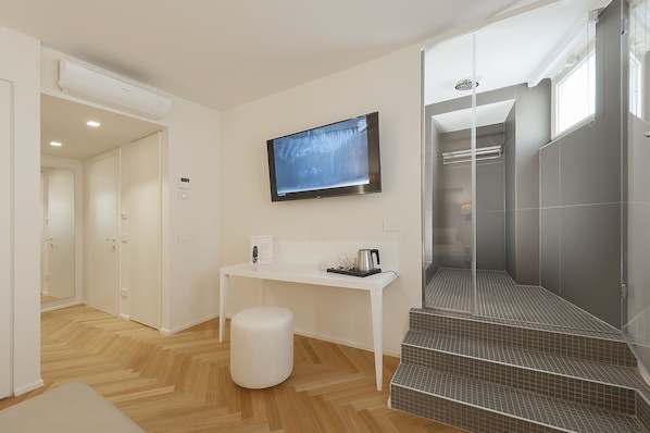 A modern bathroom with a shower, a toilet, and a sink. There is a white bench and a small table with a kettle and a cup. - Asisium Boutique Hotel (Assisi)