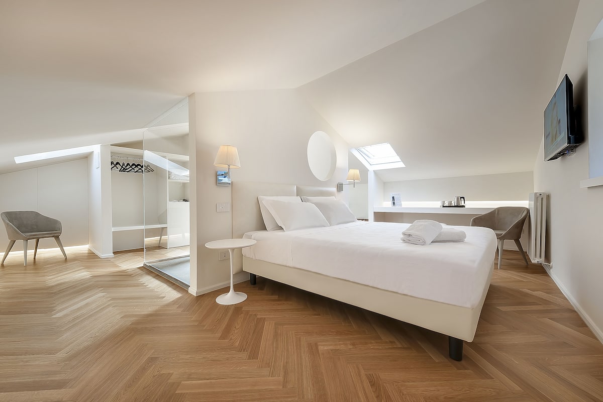 A modern hotel room with a large bed, a desk, a chair, and a walk-in closet.
