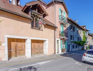 Blick auf eine Straße mit einer Reihe traditioneller Häuser, einem weißen Auto, das am Straßenrand geparkt ist, und einem strahlend blauen Himmel.