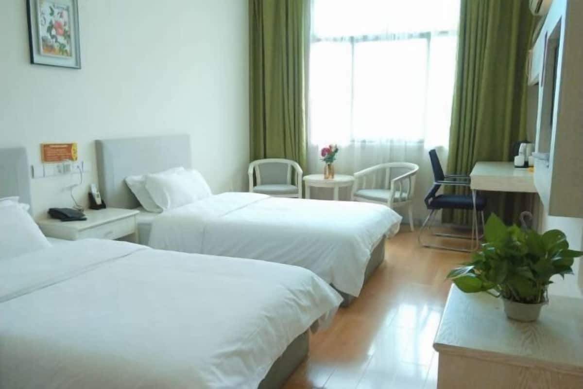 Ein Hotelzimmer mit zwei Betten, einem Schreibtisch, einem Stuhl, einem kleinen Tisch und einer Zimmerpflanze.