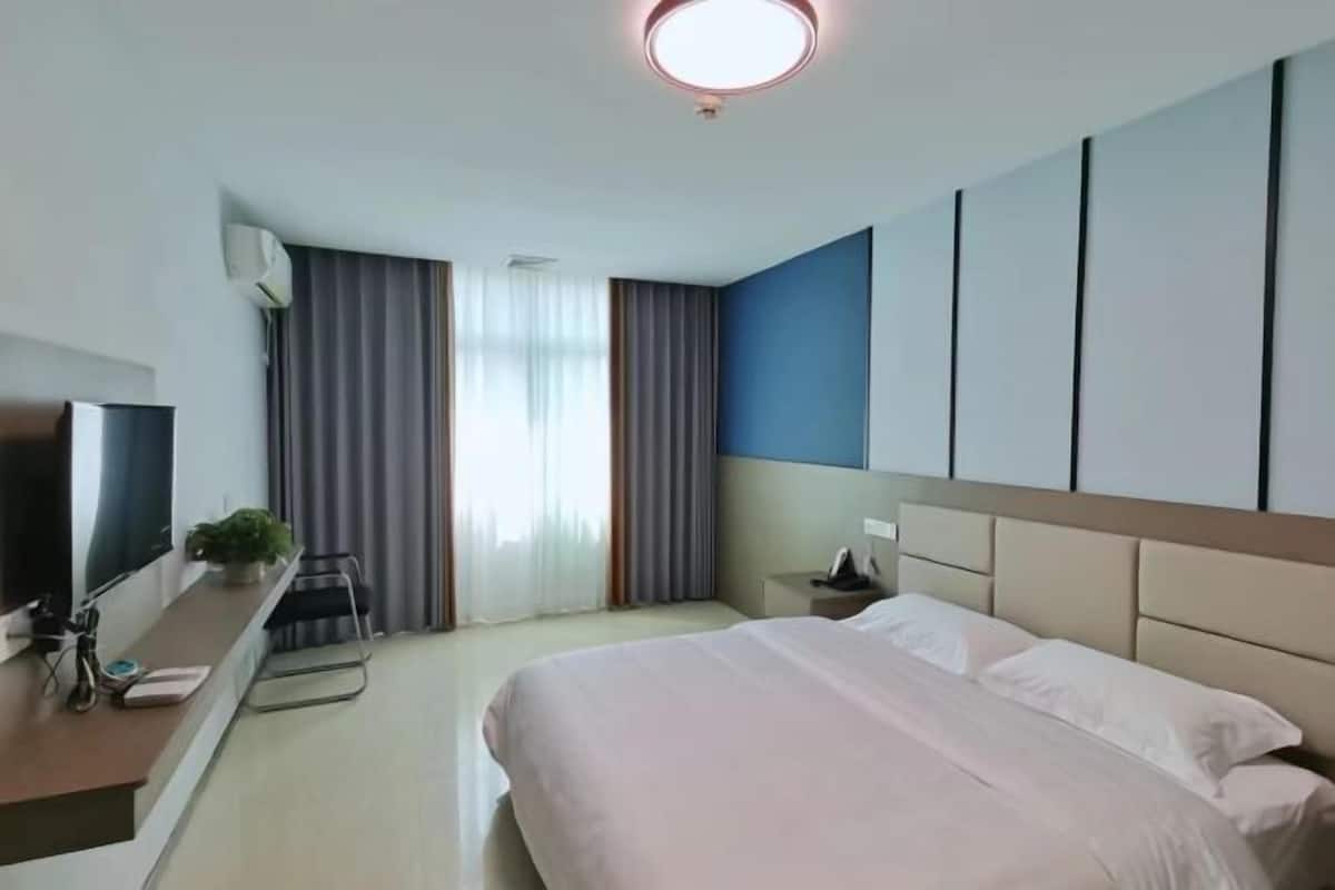 Ein Hotelzimmer mit Bett, Fernseher, Schreibtisch mit Computer und Pflanze.