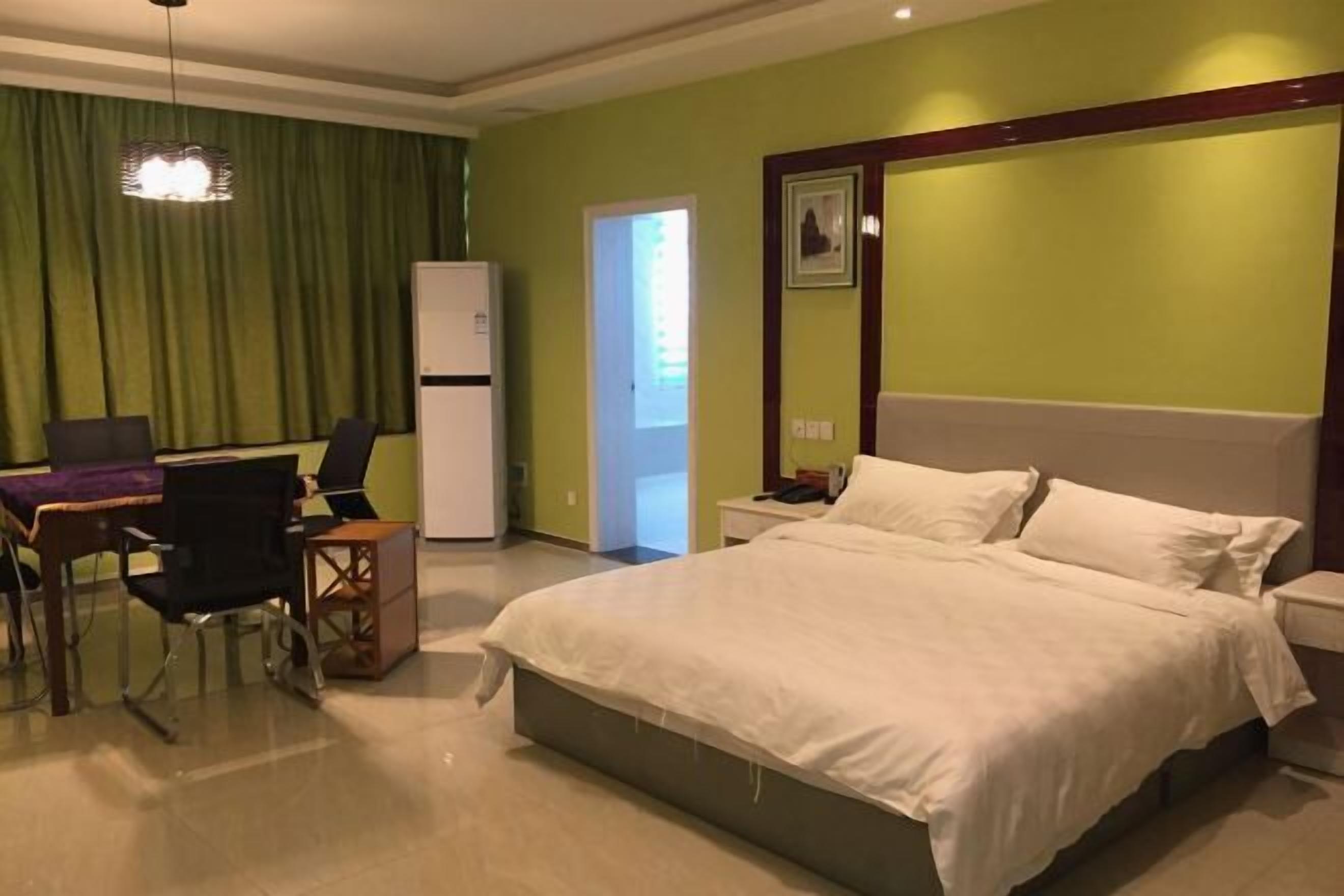 Habitación de hotel con cama, escritorio, sillas, refrigerador y puerta que da a otra habitación.