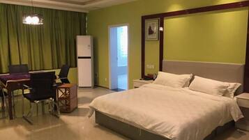 Habitación de hotel con cama, escritorio, sillas, refrigerador y puerta que da a otra habitación.