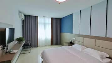A hotel room with a large bed, a desk with a chair, a television, and a window with curtains.