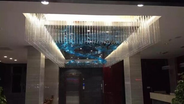 Een moderne lobby met een glazen dak, een receptiebalie en een trap naar een lift.