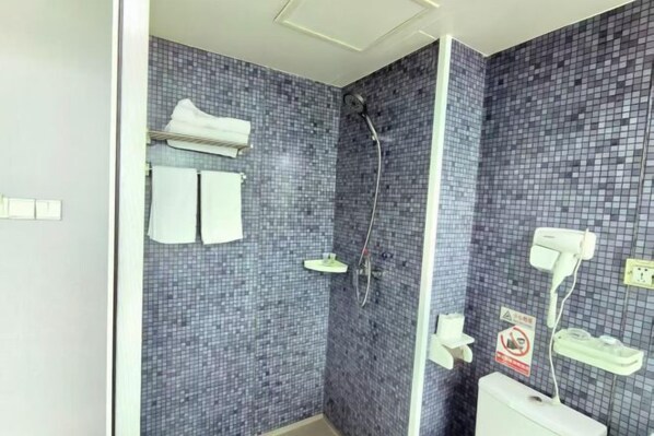 Casa de banho com chuveiro, paredes em azulejo, sanita e porta-toalhas.