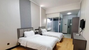 Een hotelkamer met twee bedden, een bureau, een televisie en een kledingkast.