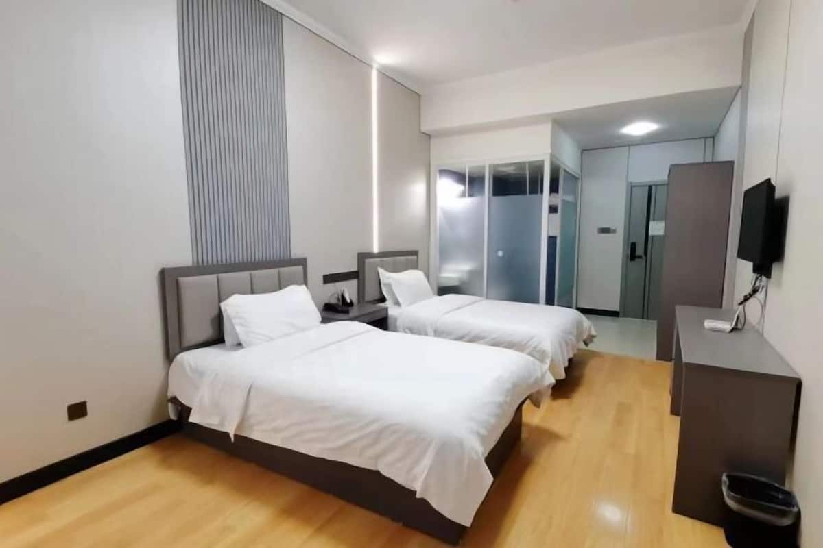 Ein Hotelzimmer mit zwei Betten, einem Schreibtisch, einem Fernseher und einem Kleiderschrank.