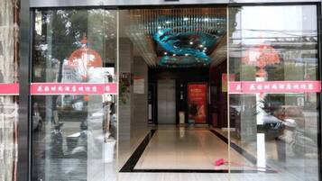 A hotel entrance with a modern glass facade, a reception desk, and a decorative ceiling feature.