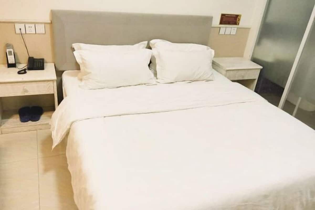 Ein Hotelzimmer mit einem Bett, zwei weißen Kissen, einem Nachttisch mit Telefon und einem kleinen Tisch mit einer Plakette.