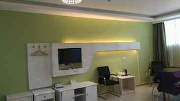 Una habitación de hotel con una televisión de pantalla plana montada en una pared blanca, un escritorio con una silla, una mesita con una silla y una cama.