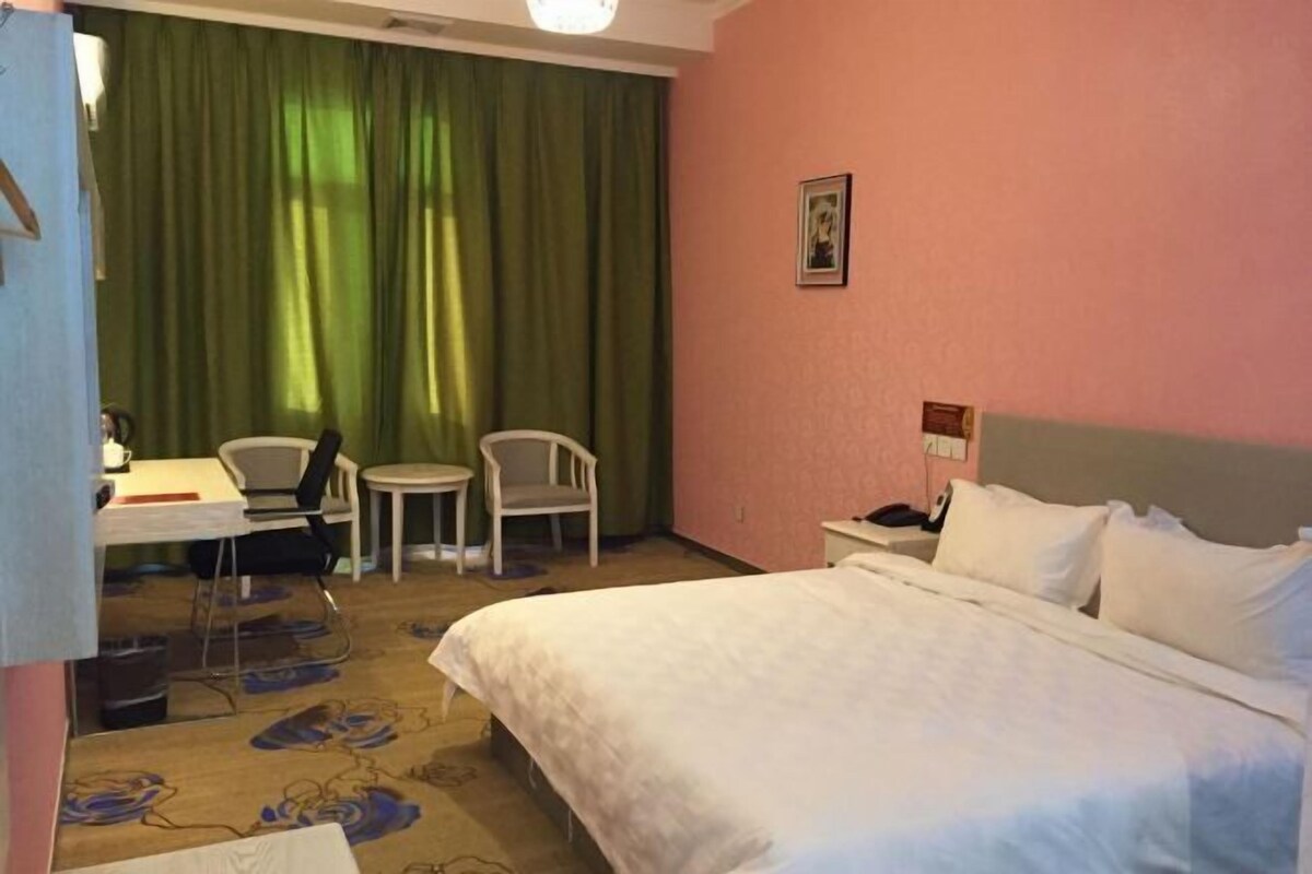 Une chambre d’hôtel avec un grand lit, un bureau avec une chaise, une petite table et un rideau vert.
