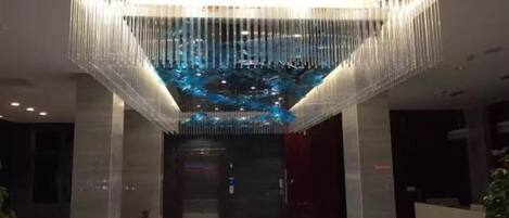 Un vestíbulo moderno con una araña central, un mostrador de recepción y una escalera que lleva a un ascensor.