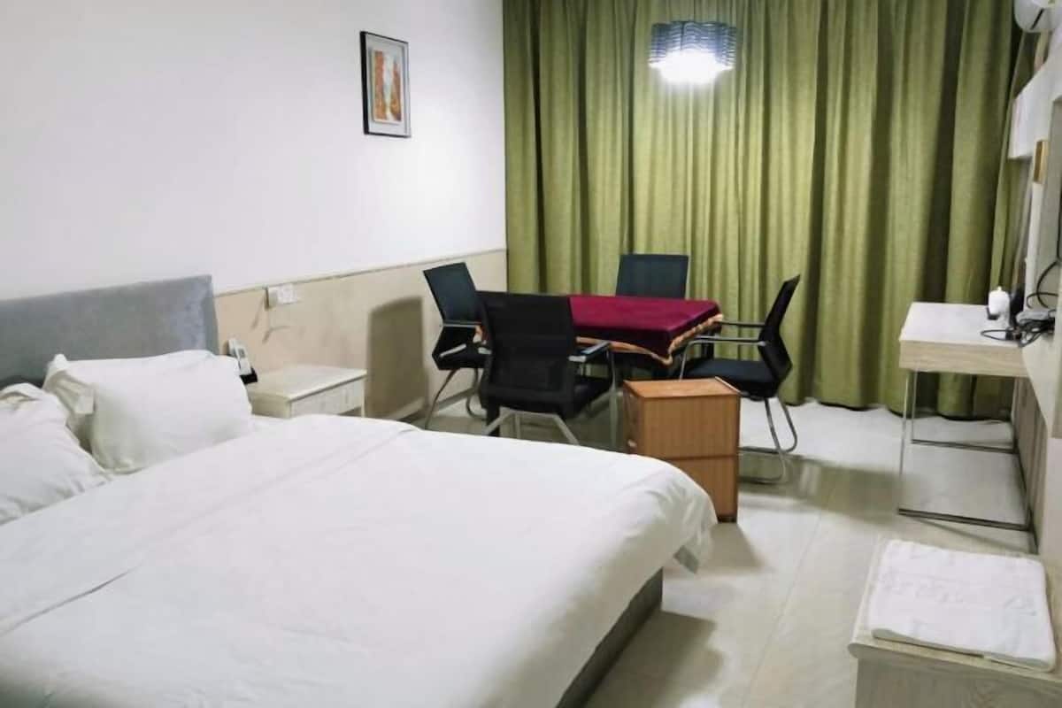 Ein Hotelzimmer mit Bett, Schreibtisch, Stuhl, Tisch und Vorhang.