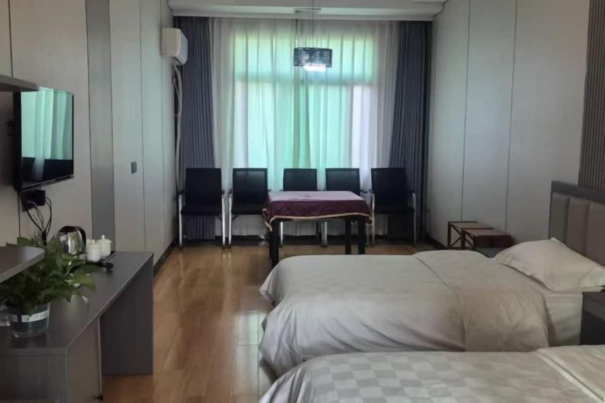 Ein Hotelzimmer mit zwei Betten, einem Schreibtisch mit Fernseher, einem Esstisch mit Stühlen und einem Fenster mit Vorhängen.