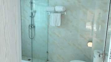 A bathroom with a glass-enclosed shower, a toilet, and a towel rack with two towels.