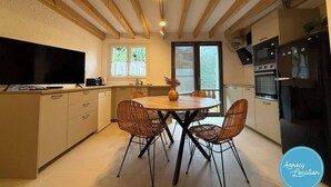 A modern kitchen with wooden beams, a dining table with chairs, a TV, and built-in appliances. - The Bergerie T3- view Mountains. (Talloires-Montmin)