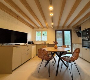 Eine moderne Küche mit Holzbalken, einem Esstisch mit Stühlen, einem Fernseher und Einbaugeräten.