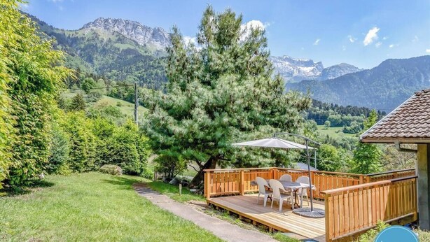 A deck with outdoor seating, surrounded by lush greenery and mountains in the background. - The Bergerie T3- view Mountains. (Talloires-Montmin)