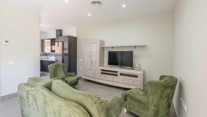 A modern living room with a flat-screen TV, green upholstered sofas, a cabinet, and a kitchen in the background. - Torero II Apartment - Marchena (Marchena)