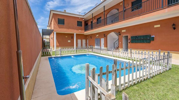 A swimming pool with a wooden fence, a covered walkway, and a building with balconies and mailboxes. - Torero II Apartment - Marchena (Marchena)