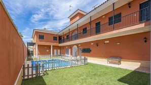A courtyard with a swimming pool, a grassy lawn, and a building with balconies and a fence. - Torero II Apartment - Marchena (Marchena)