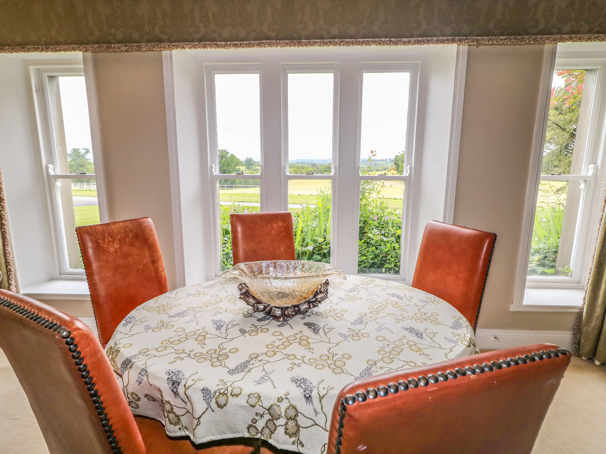 Een eettafel met een tafelkleed met bloemenprint, omringd door vier stoelen met decoratieve randen.